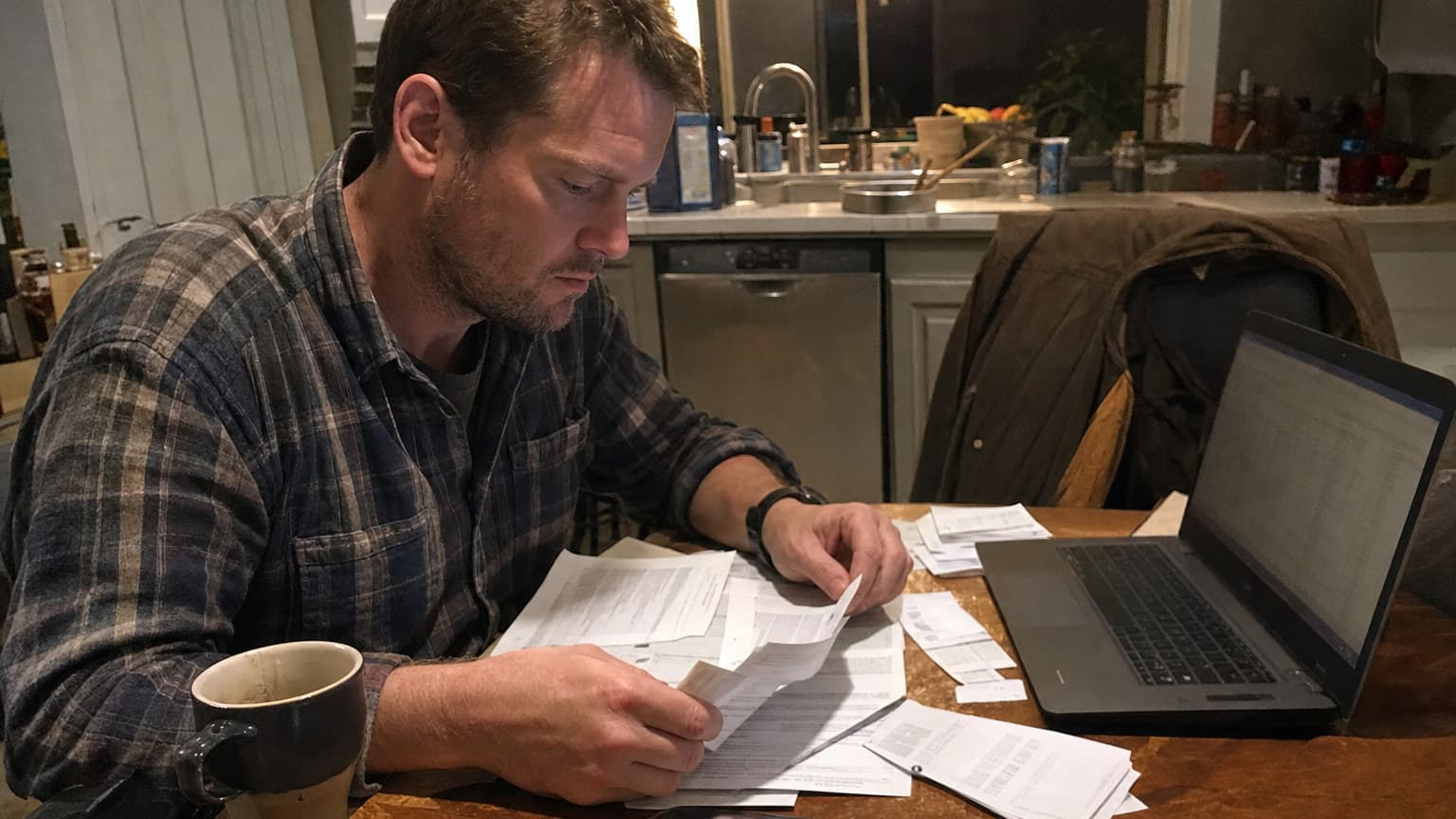 A buyer sitting at a kitchen table counting out savings and loan paperwork while working out the cash needed to close on a small trades business